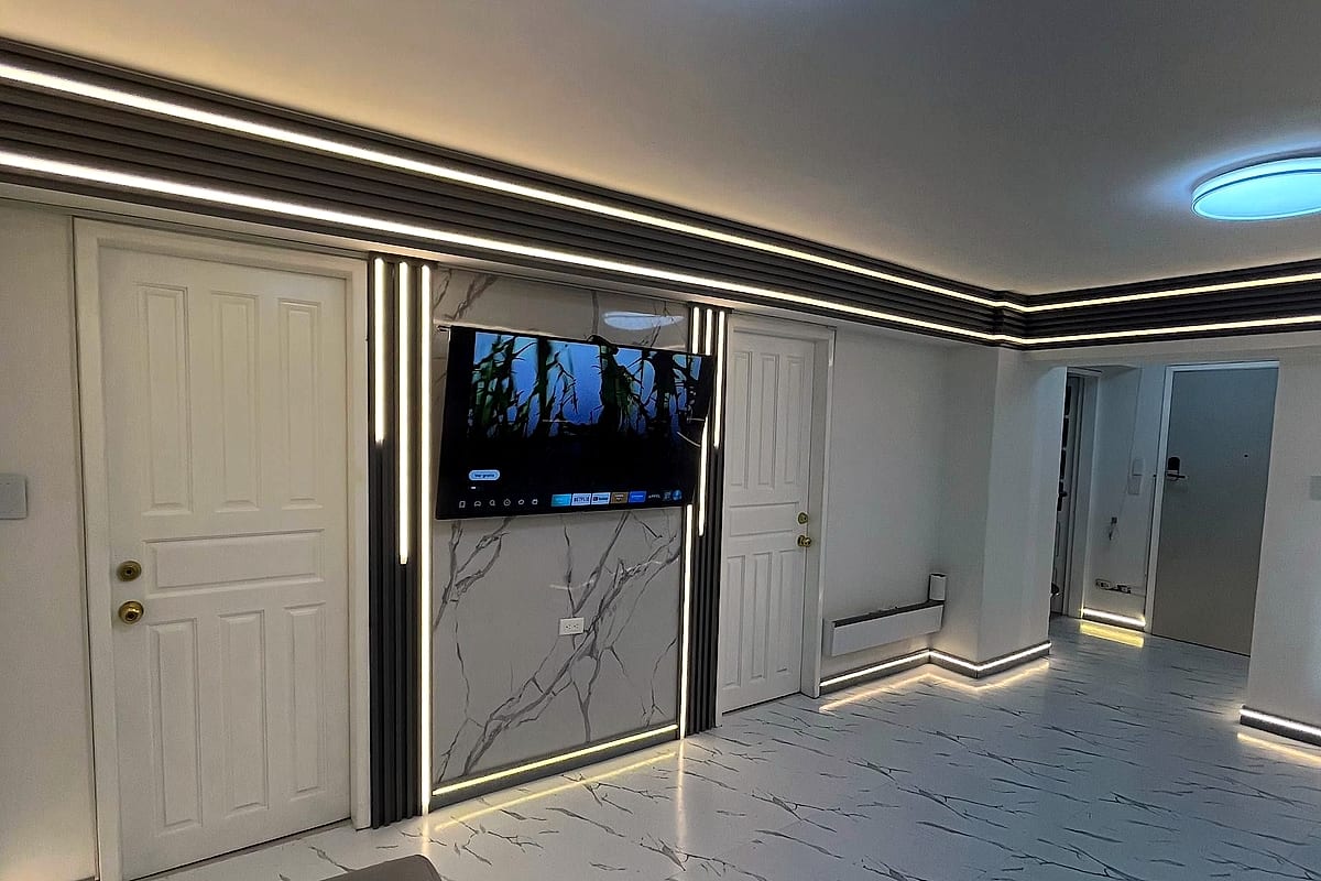 Pared revestida en mármol con televisor y molduras LED verticales