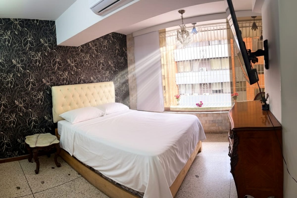 Habitación con cabecero capitoné y ventanal hacia la ciudad en Chacao, Caracas