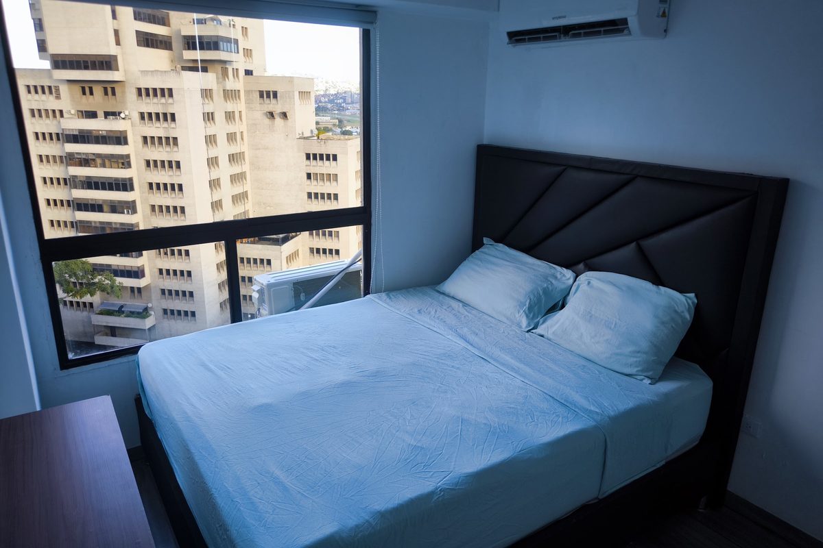 Habitación con cama doble y ventanal hacia los edificios de Bello Campo, Chacao